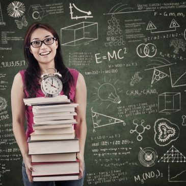 asian student is holding stack of books and clock in the classroom