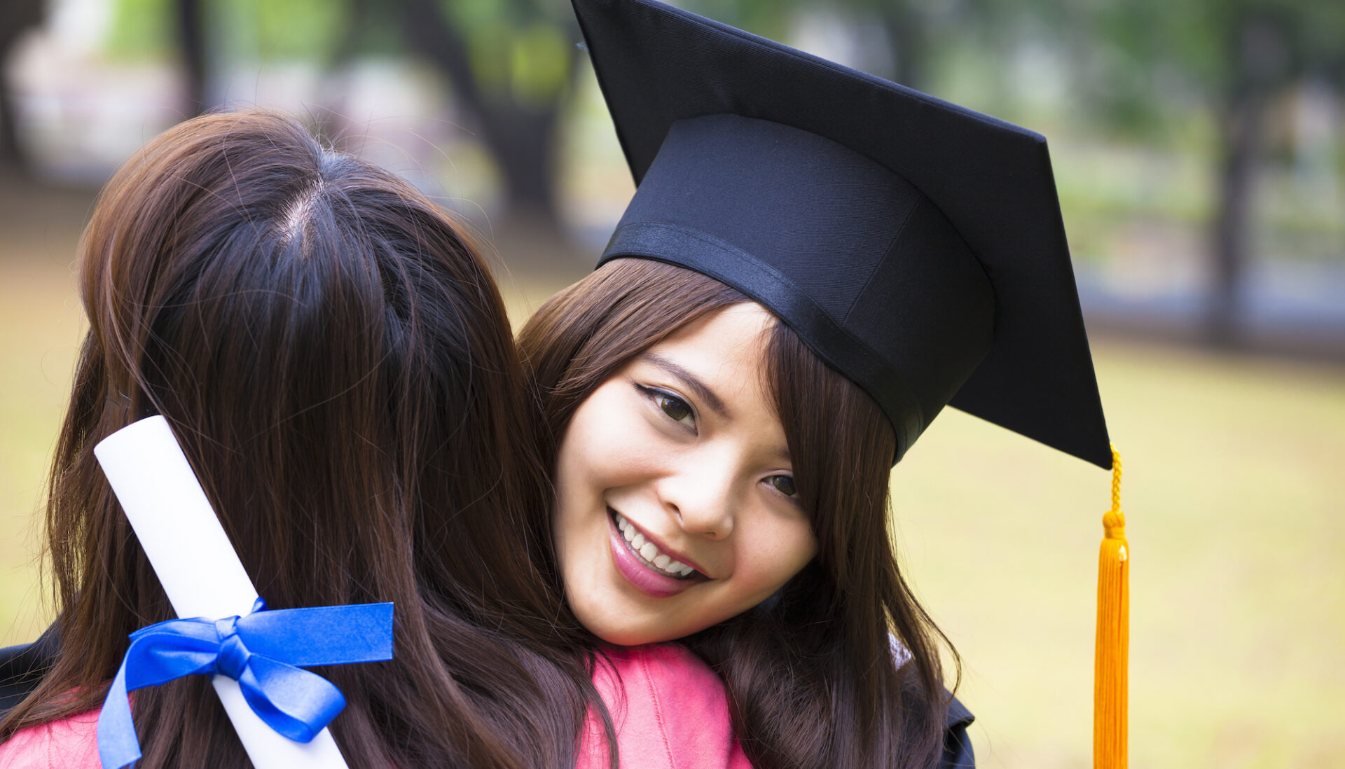 Finance Tips For Graduates | Camino Federal Credit Union | young female graduate hugging her friend at graduation ceremony