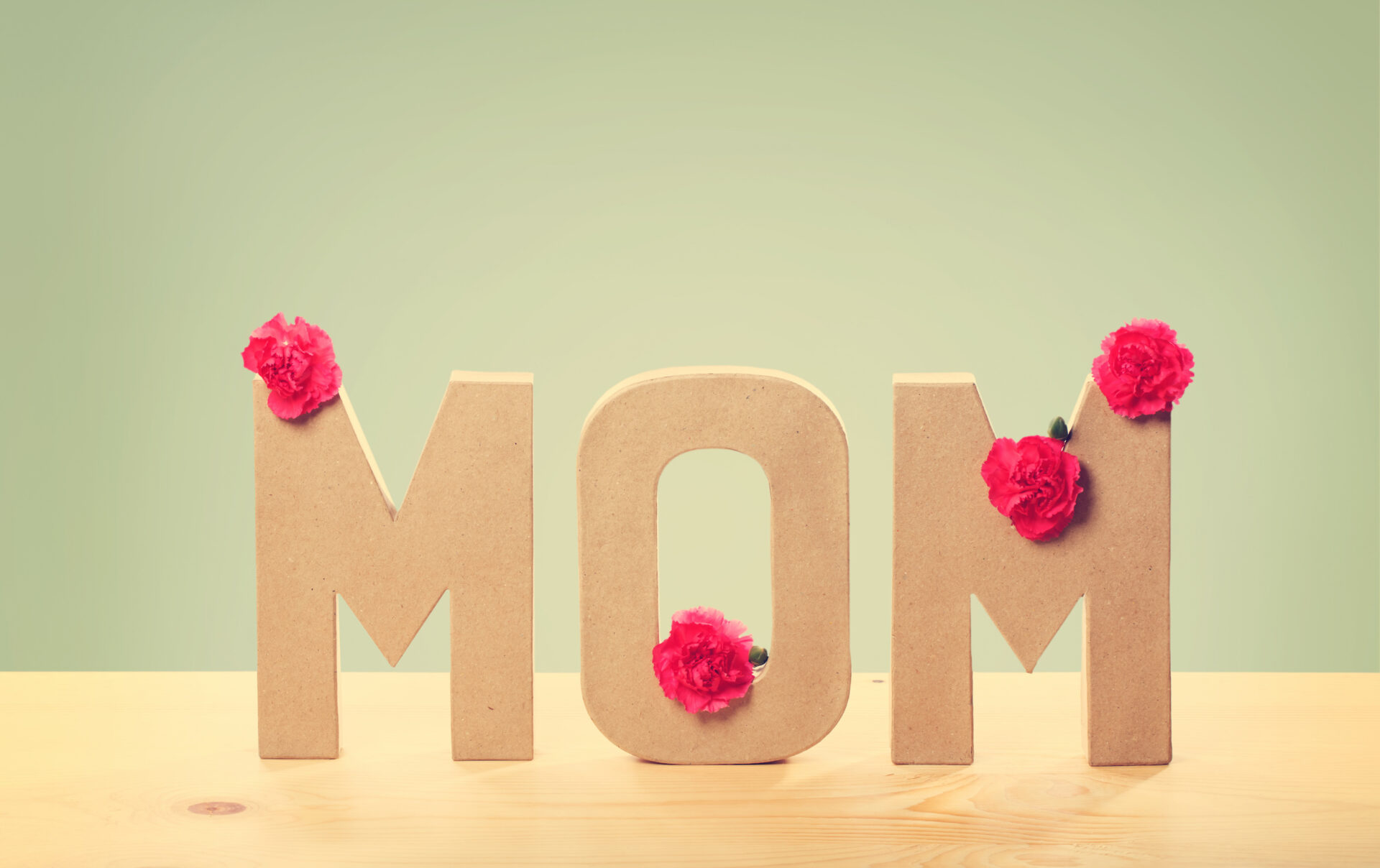 Mother's Day Ideas | Camino Federal Credit Union | Three Dimensional Text That Says Mom with Fresh Carnation Flowers Standing on the Wooden Table with Light Green Background