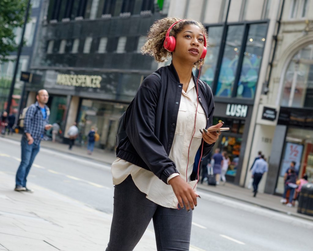 young woman walking through city with headphones and backpack