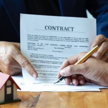 A borrower signs a mortgage contract with a toy house to the side