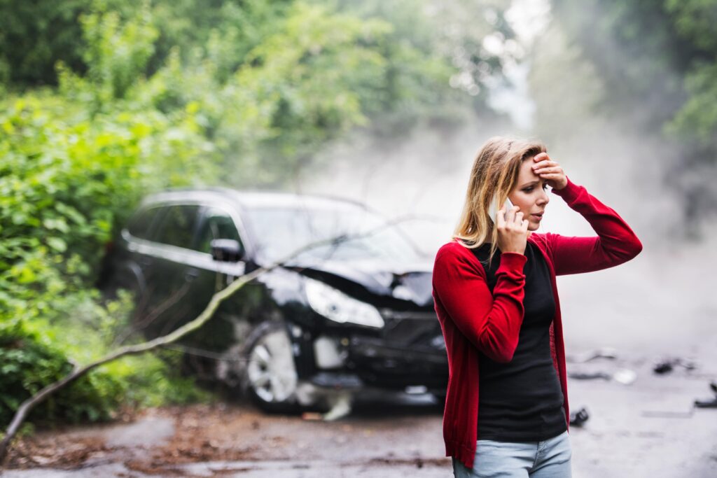 A woman with a hand to her head makes a call next to her wrecked car. 