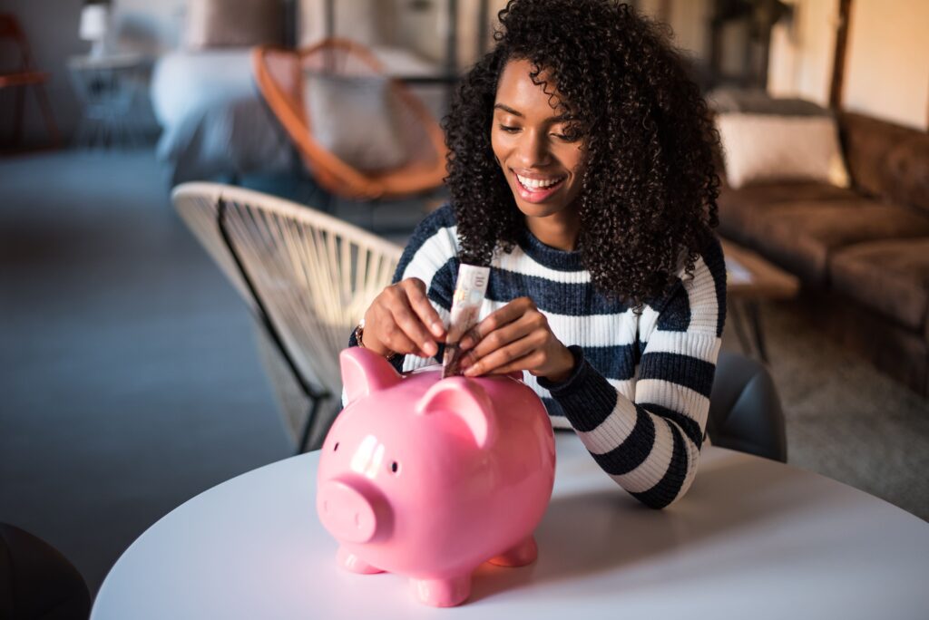 a woman puts a folded dollar bill into a piggy bank