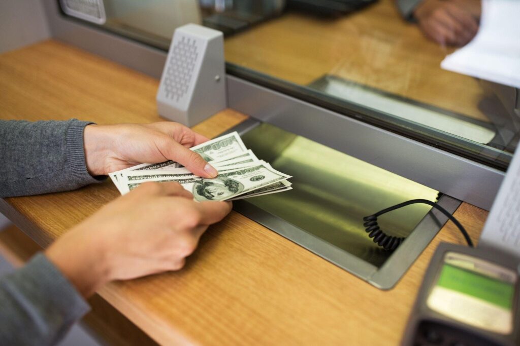 a person at a bank teller window hands over cash